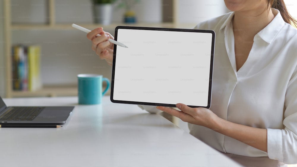 Frau im weißen Hemd präsentiert digitales Tablet mit Mock-up-Bildschirm und mit Stift, der auf den Bildschirm zeigt