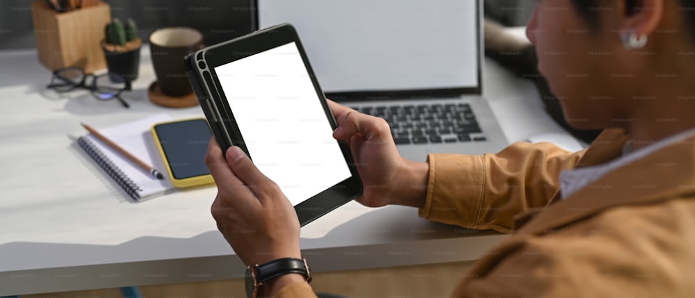 Over shoulder closeup view of businessman holding digital tablet with blank screen.