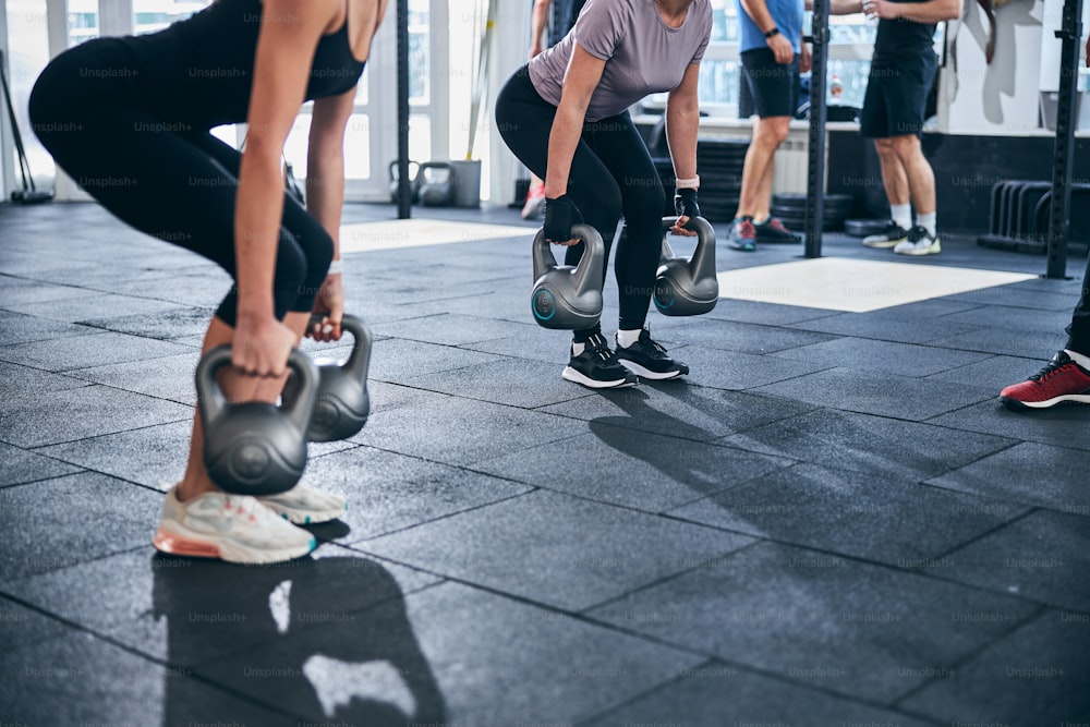 Cropped photo of two athletic women performing the dual kettlebell deadlift in a fitness studio