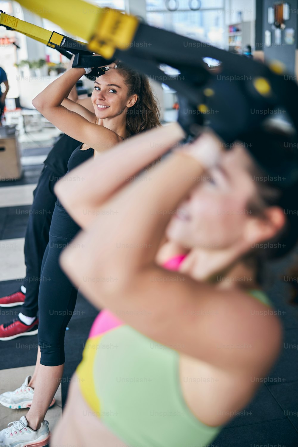 Mujer hermosa sonriente haciendo un ejercicio de curl de bíceps con sus compañeros de fitness en el gimnasio