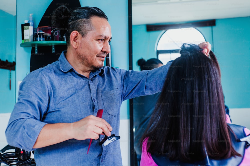 Hombre latino que trabaja como peluquero y corta el cabello de una clienta en un salón de belleza pequeña empresa en la ciudad de México