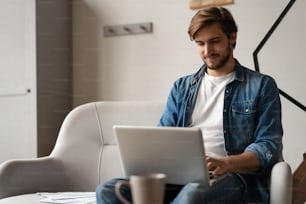 Entrepreneur prospère souriant de satisfaction alors qu’il vérifie des informations sur son ordinateur portable tout en travaillant dans un bureau à domicile