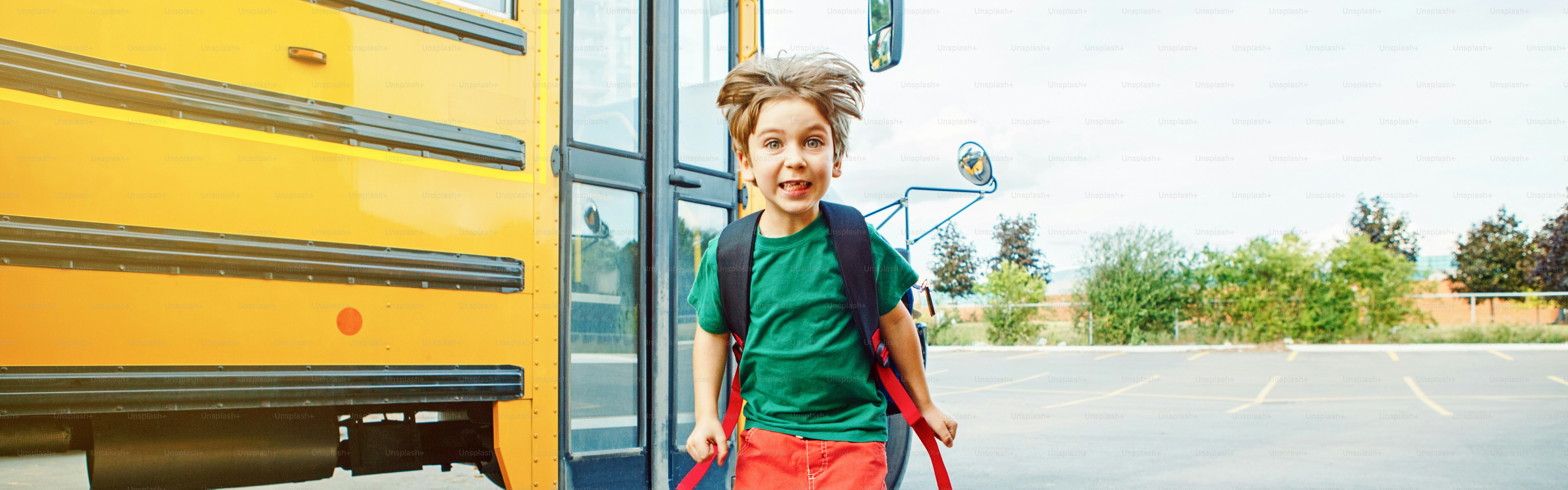 Niño estudiante caucásico emocional con expresión facial divertida saltando cerca del autobús amarillo el día 1 de septiembre. Regreso a la escuela de la educación. Niño listo para aprender, estudiar. Encabezado de banner web para sitio web.