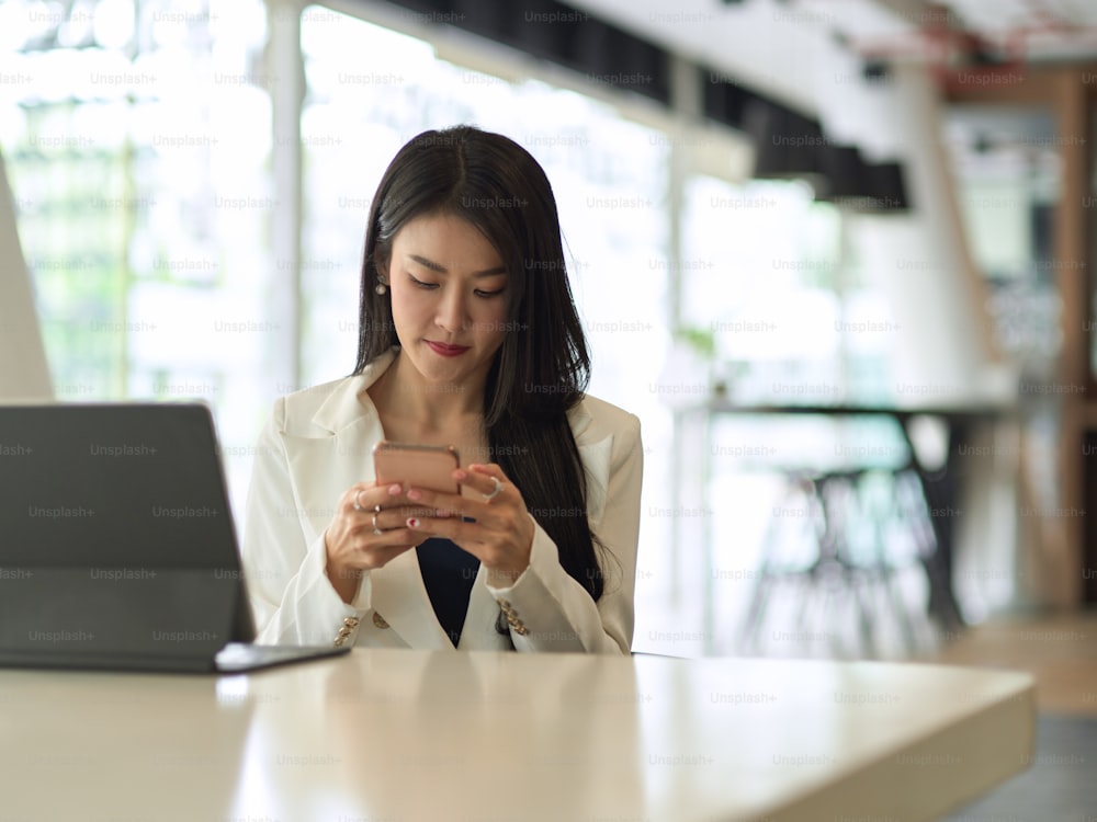 Porträt einer Geschäftsfrau, die mit Smartphone und digitalem Tablet in einem modernen Büroraum arbeitet