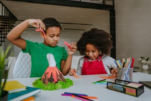 Schwester und Bruder haben Spaß daran, DIY-Vulkanmodell von Kindern zu machen, spielen Ton für das Schulprojekt. Konzept für Heimerziehung.