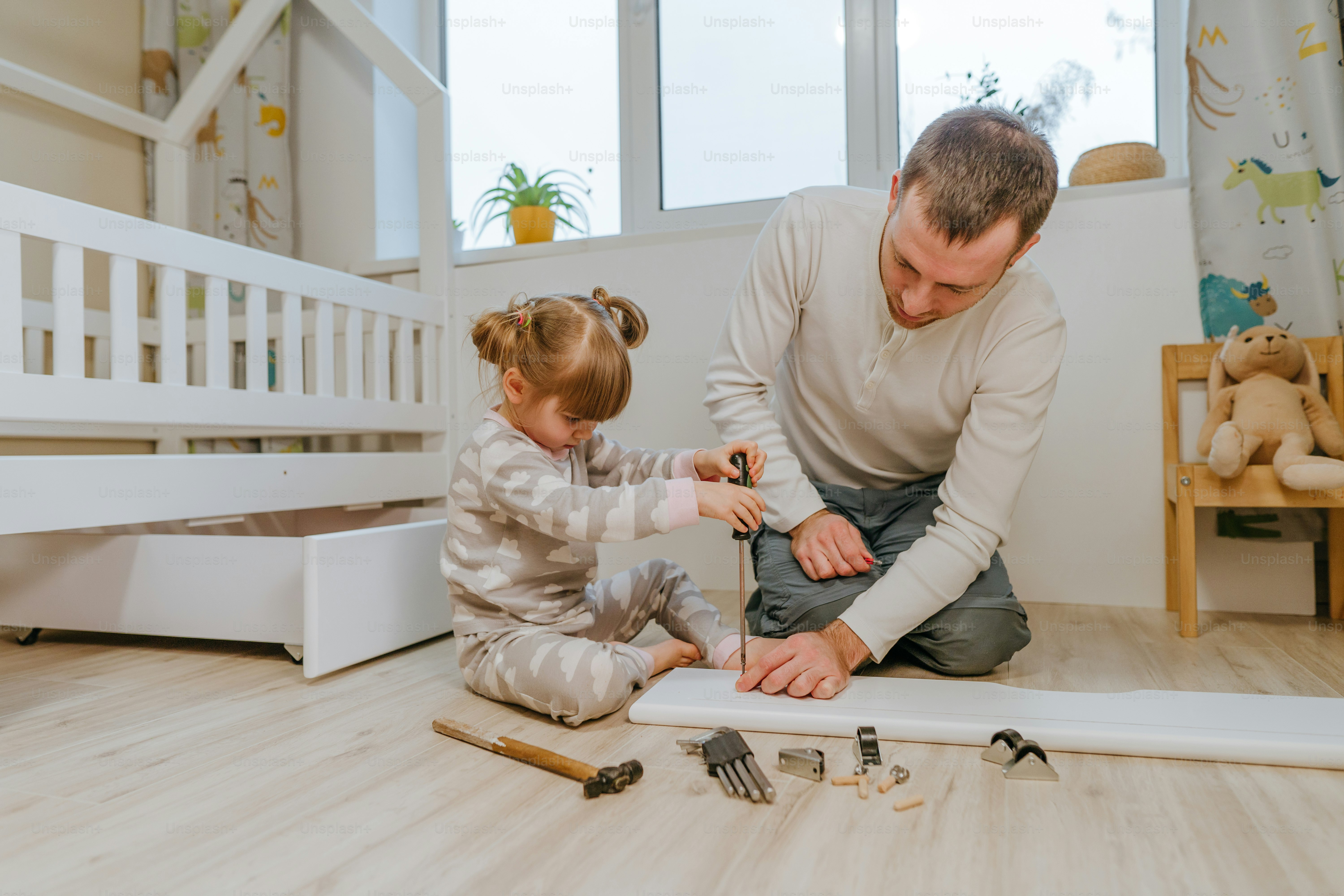 Little 4-years girl helps her father assemble or fixing the drawer of bed in the kids bedroom.