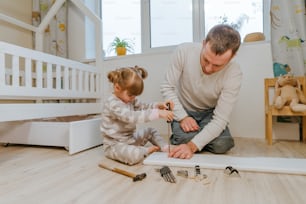 Little 4-years girl helps her father assemble or fixing the drawer of bed in the kids bedroom.