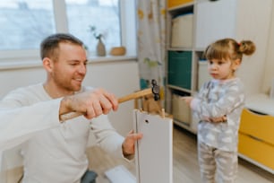 子供部屋で4歳の娘にハンマーの使い方を教える父親。ハンマーに選択的に焦点を合わせます。