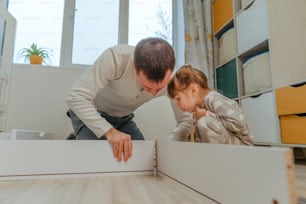 Little 4-years girl helps her father assemble or fixing the drawer of bed in the kids bedroom.