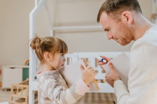 어린 4 살 소녀는 아버지가 어린이 침실에서 침대 서랍을 조립하거나 고정하는 것을 돕습니다.