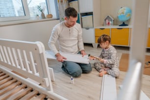 子供の寝室で小さなハンマーを使って父親が子供用ベッドを組み立てるのを手伝う小さな4歳の女の子。