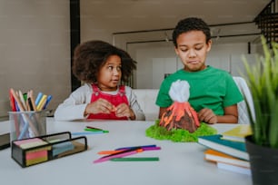 Schwester und Bruder haben Spaß daran, DIY-Vulkanmodell von Kindern zu machen, spielen Ton für das Schulprojekt. Konzept für Heimerziehung.