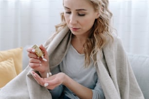 Sick woman covered with blanket holding capsule pills in hand. Concept of medicine for immunity during the global coronavirus covid-19 pandemic and quarantine. Health care and treatment