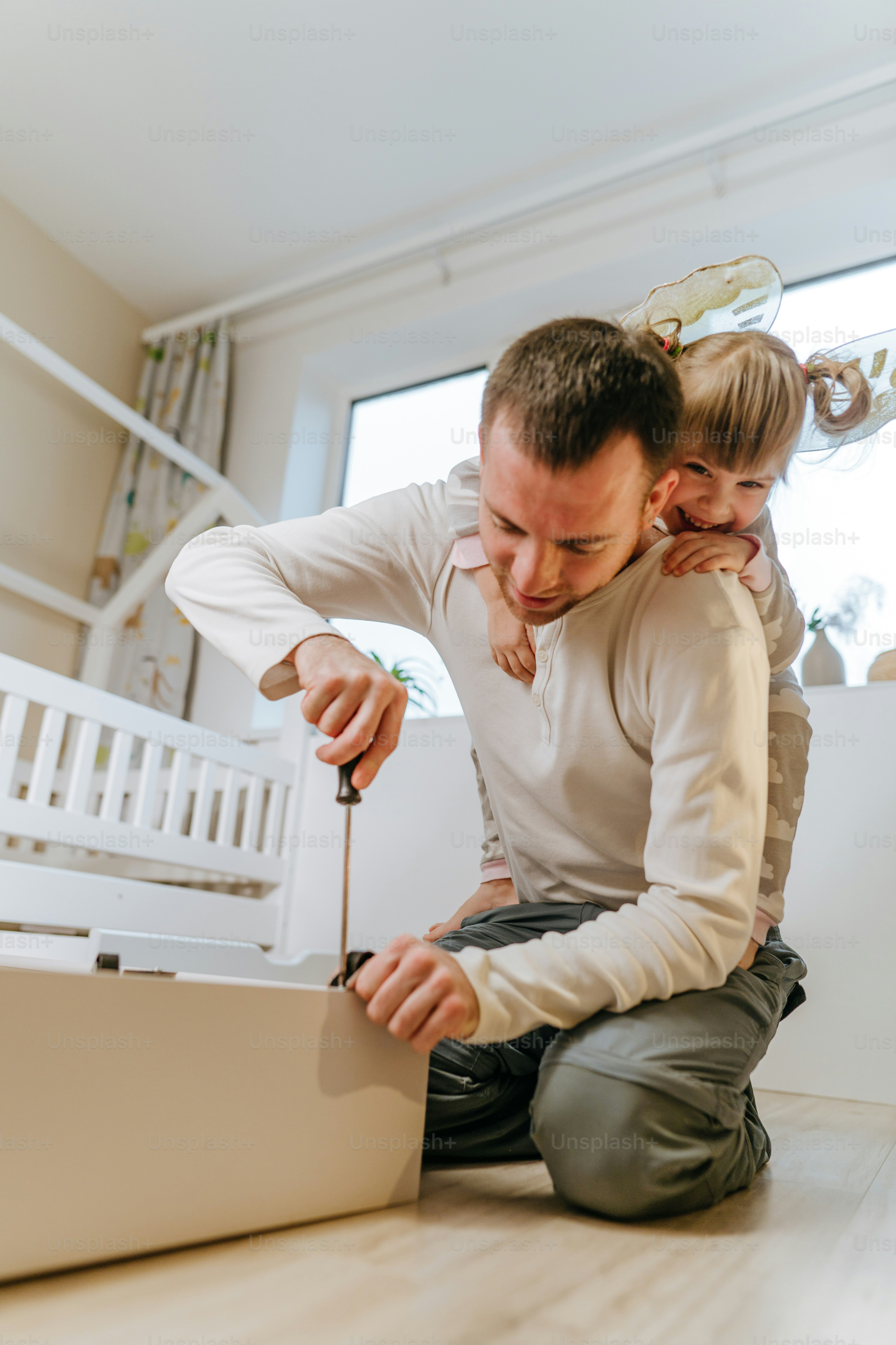 Little 4-years girl helps her father assemble or fixing the drawer of bed in the kids bedroom.