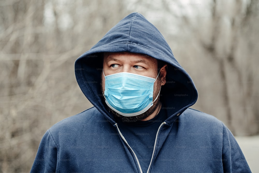 백인 젊은 중년 남자가 야외에서 위생 얼굴 마스크를 쓰고 있습니다. 바이러스의 위험한 확산으로부터 보호하는 사람. 코로나바이러스 COVID-19 호흡기 질환 검역소.