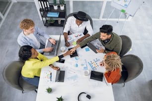 Competent IT specialists in stylish outfit working on modern gadgets while sitting together at bright office. Young multiracial people shaking hands, talking and smiling during cooperation.