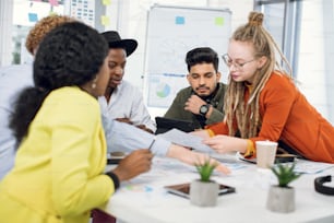 Cinque freelance multietnici che lavorano insieme in un ufficio luminoso e utilizzano gadget moderni. Giovani studenti hipster che creano una strategia aziendale di progetto comune.