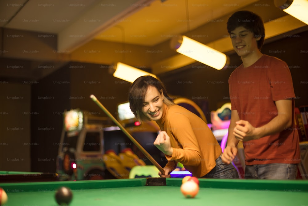Young couple spending time in billiard room. Woman is a winner. Focus is on couple.