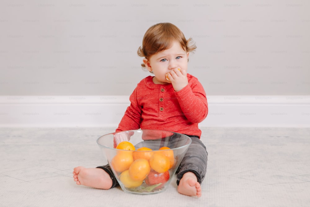 Cute adorable Caucasian baby boy eating citrus fruit mandarine orange. Finny child eating healthy organic snack tangerine. Solid finger food and supplementary food for children toddlers.