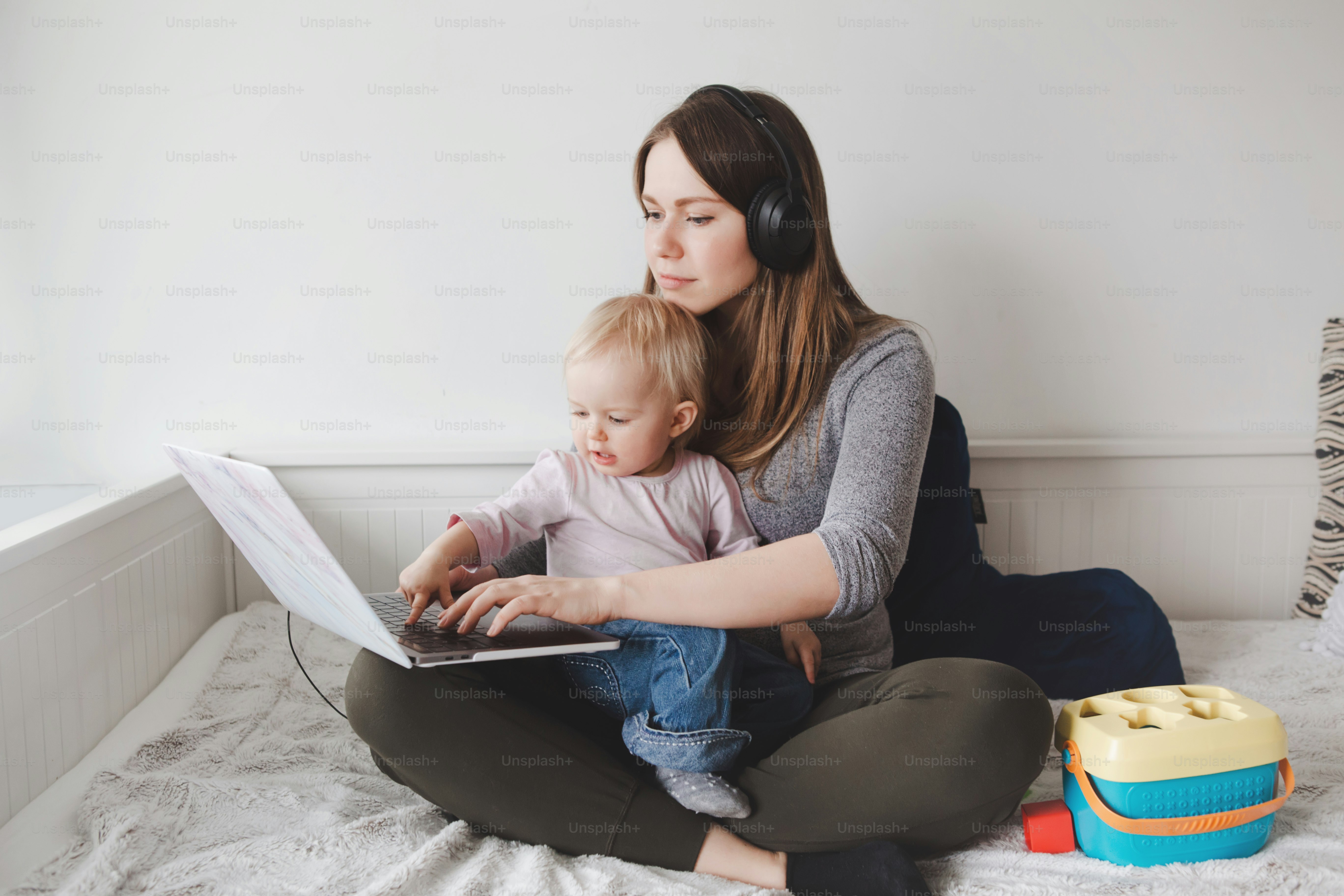 Caucasian mother blogger with baby working on laptop from home. Workplace of freelance woman with kid toddler. Stay at home single mom earning money at online remote distant job.
