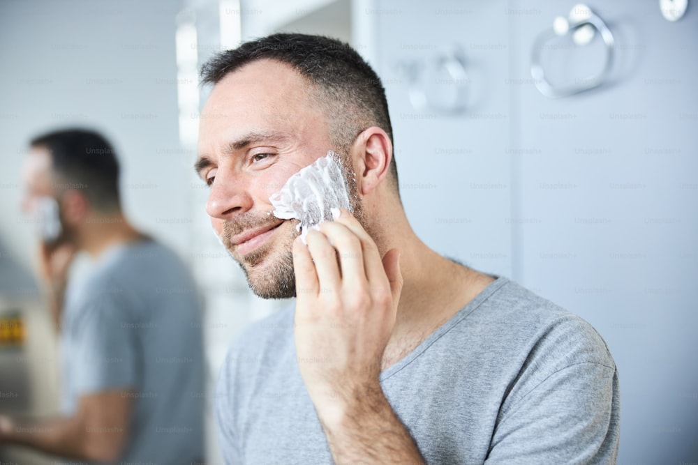 Caballero guapo mirándose en el espejo y sonriendo mientras prepara la piel para el afeitado