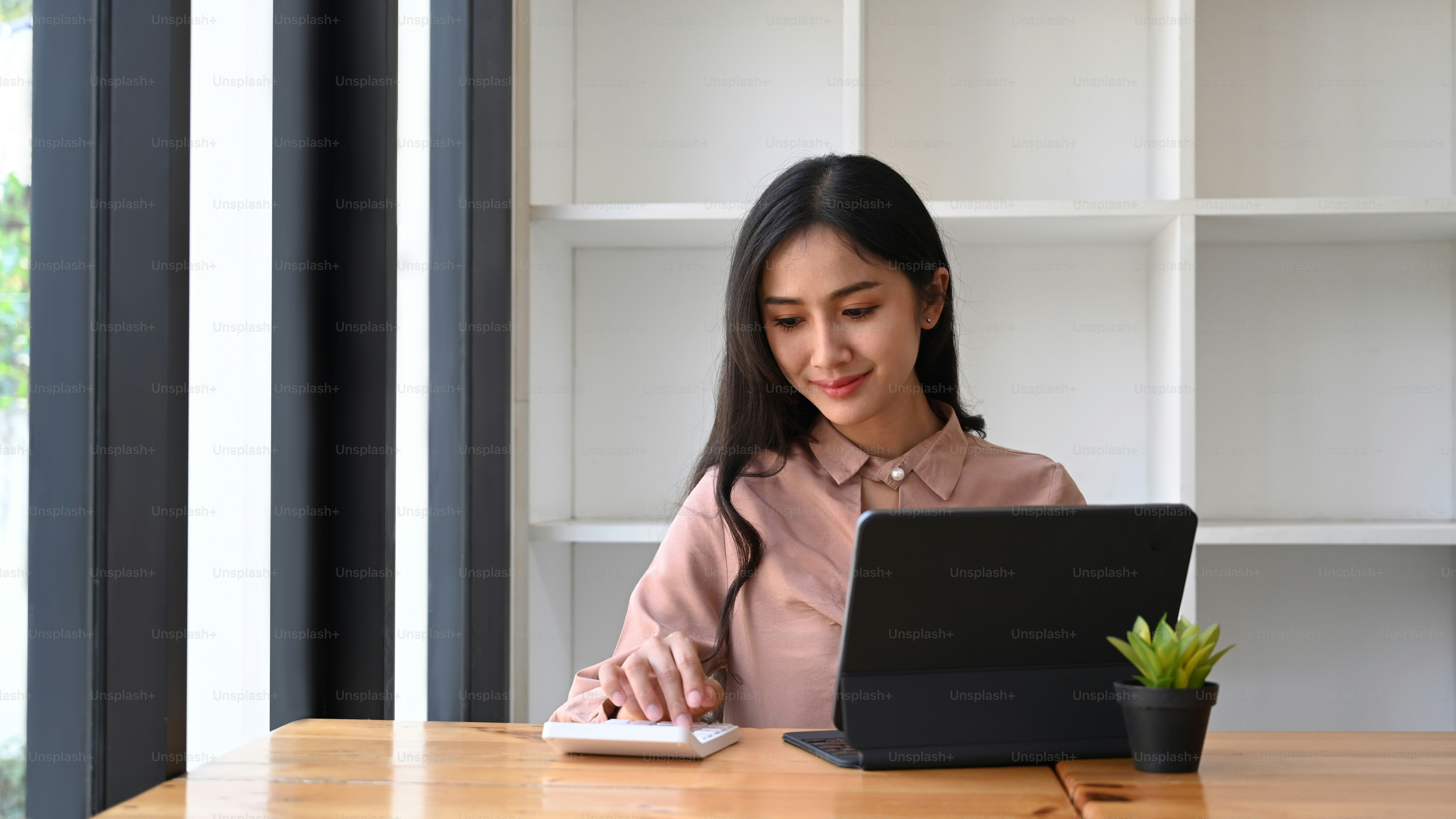 Smiling woman accountant working with computer table and using calculator calculating business data at office.