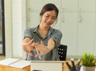 快適なオフィスルームで仕事をしながら腕を伸ばしてリラックスする女性サラリーマンのハーフレングスポートレート