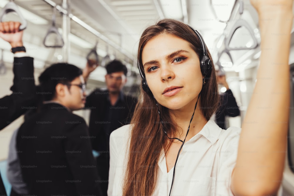 Belle jeune femme passagère debout avec des écouteurs et une chemise dans la rame de métro moderne