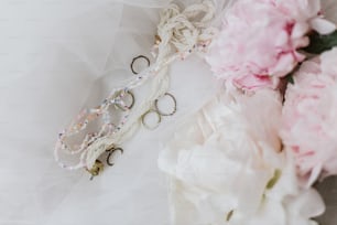 Elegantes accesorios vintage en suave tejido de tul con ramo de peonía. Hermosas joyas modernas y flores de peonía rosas y blancas. Mañana nupcial. Esenciales femeninos