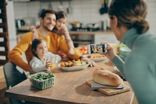 Close-up of woman taking picture of her husband and daughters at dining table.
