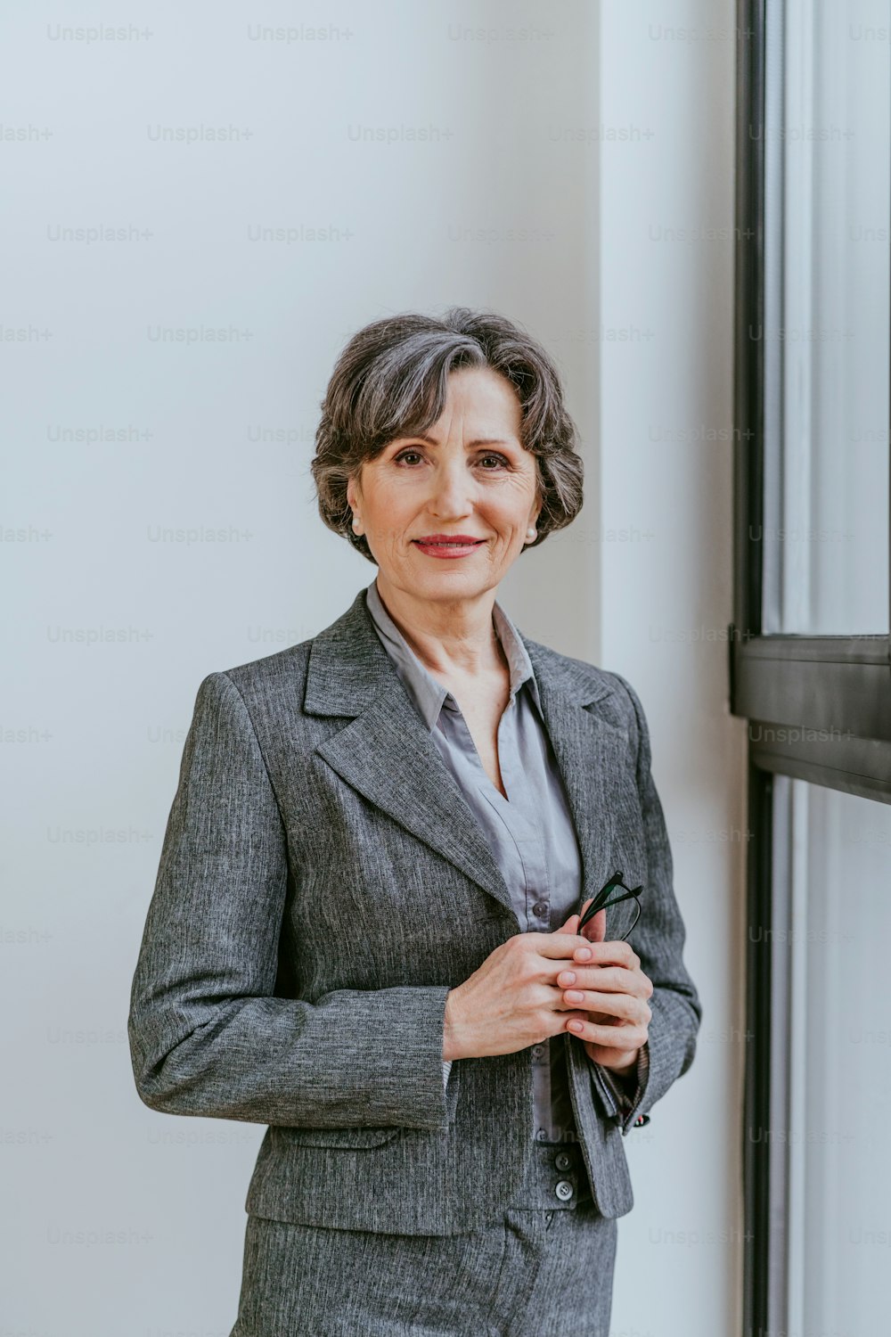 Portrait of mature businesswoman looking at camera standing in an office  near the window indoor. photo – Suit Image on Unsplash