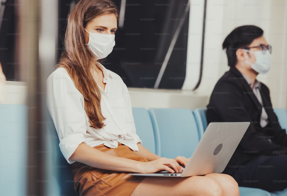 働く女性がノートパソコンを操作し、衛生的なマスクを着用し、スカイトレイン駅でコロナウイルスを予防