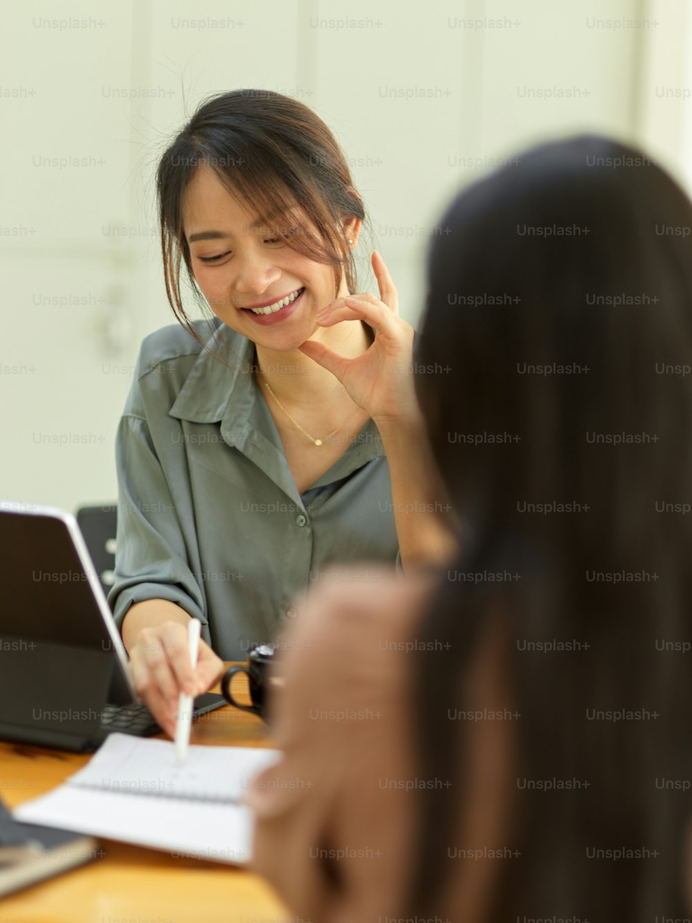 Foto cortada de trabalhadoras sorridentes conversando com colega e apontando para um caderno em branco na sala de reuniões
