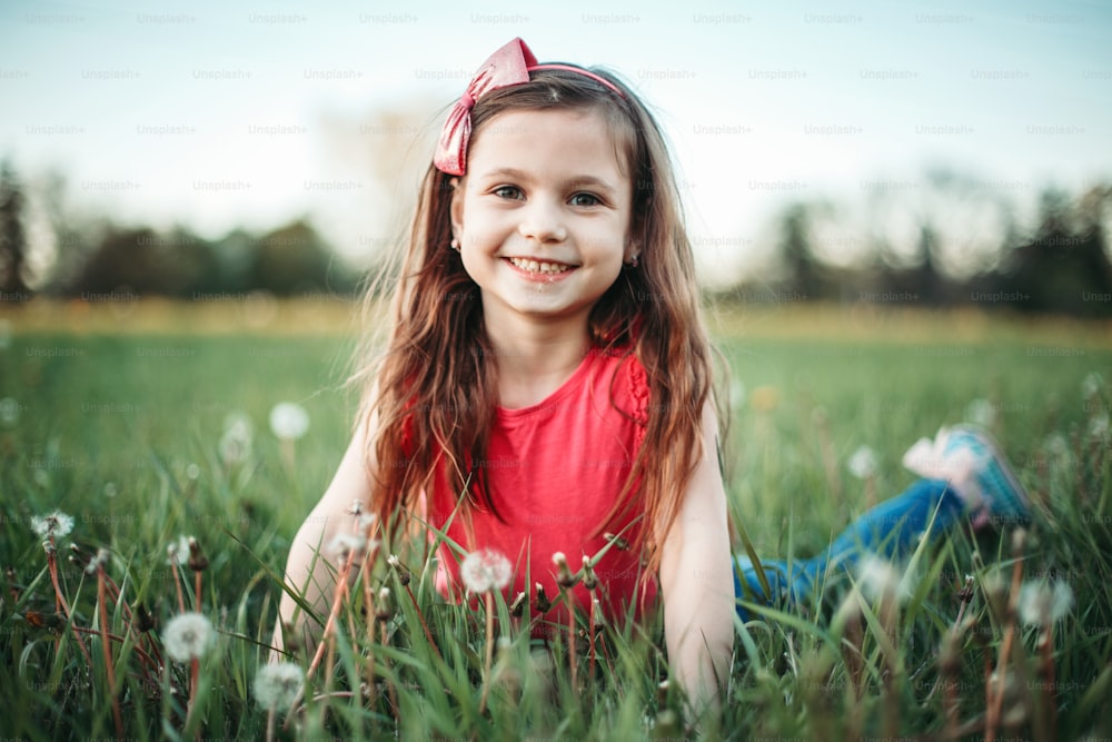 민들레 꽃 사이에 귀여운 사랑스러운 백인 소녀. 초원의 풀밭에 누워있는 아이. 야외 활동 여름 계절 어린이 활동. 밖에서 즐거운 시간을 보내는 아이. 행복한 어린 시절 생활 방식.