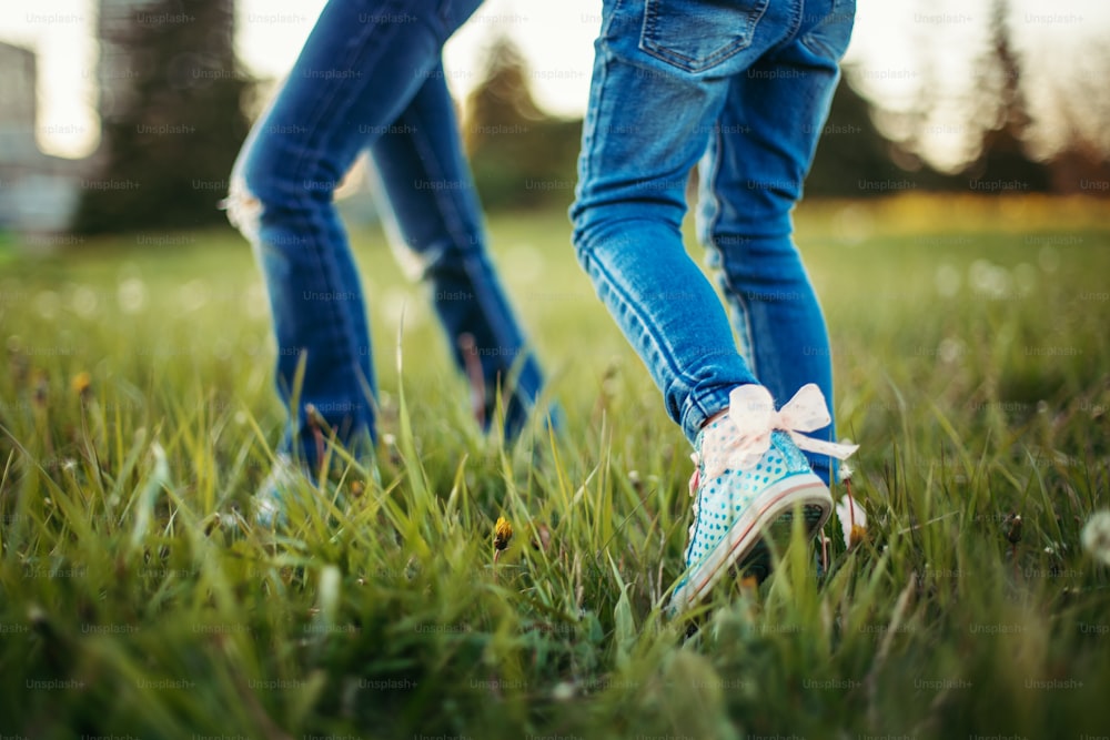 Children friends walking on meadow. Closeup of kids legs in jeans on grass. Outdoor fun summer seasonal children activity. Friends having fun together. Happy childhood lifestyle.