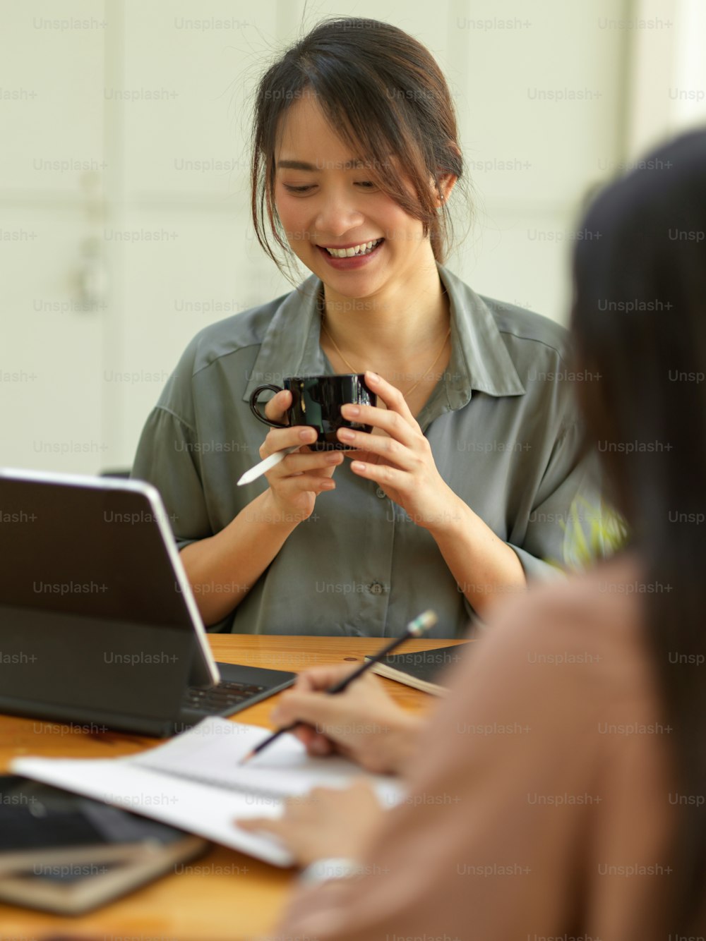 Cropped shot of smiling female holding cup while sitting opposite her coworker in office room