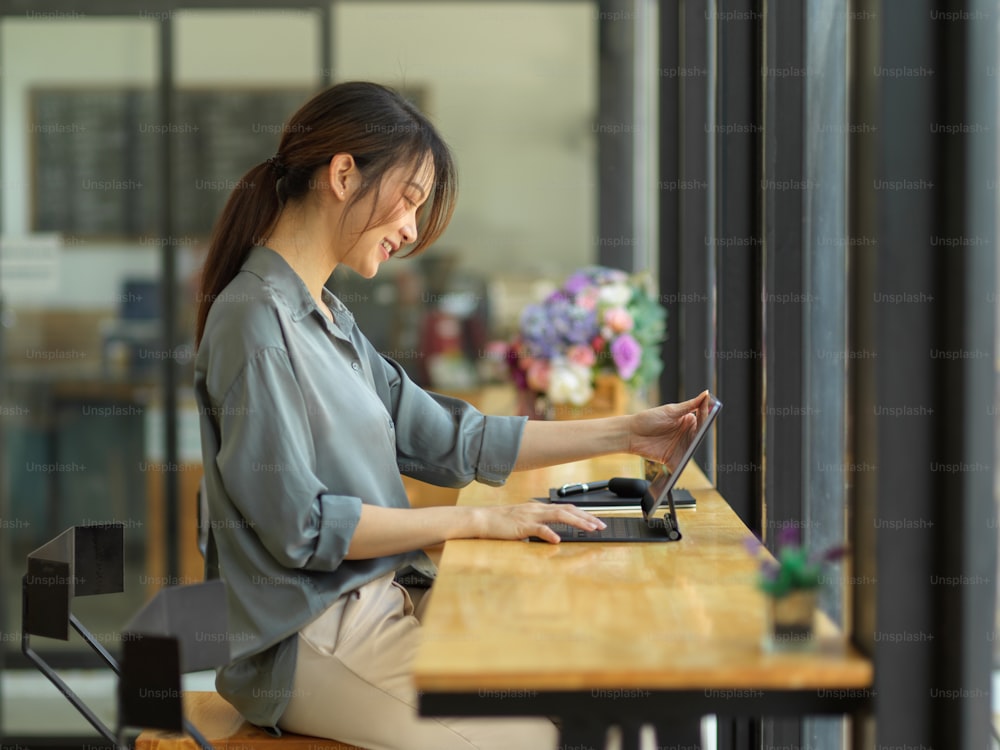 Side view of female worker using digital tablet on wooden bar in coffee shop