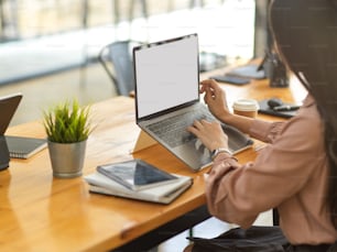 Side view of businesswoman working with laptop and office supplies on wooden table in office room