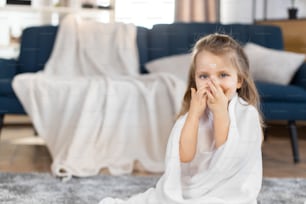 Cosméticos para niños, crema facial, concepto de cuidado de la piel. Adorable niña sonriente después del baño, con crema en la cara, copiando el comportamiento de mamá, usando crema cosmética en casa. Espacio de copia.