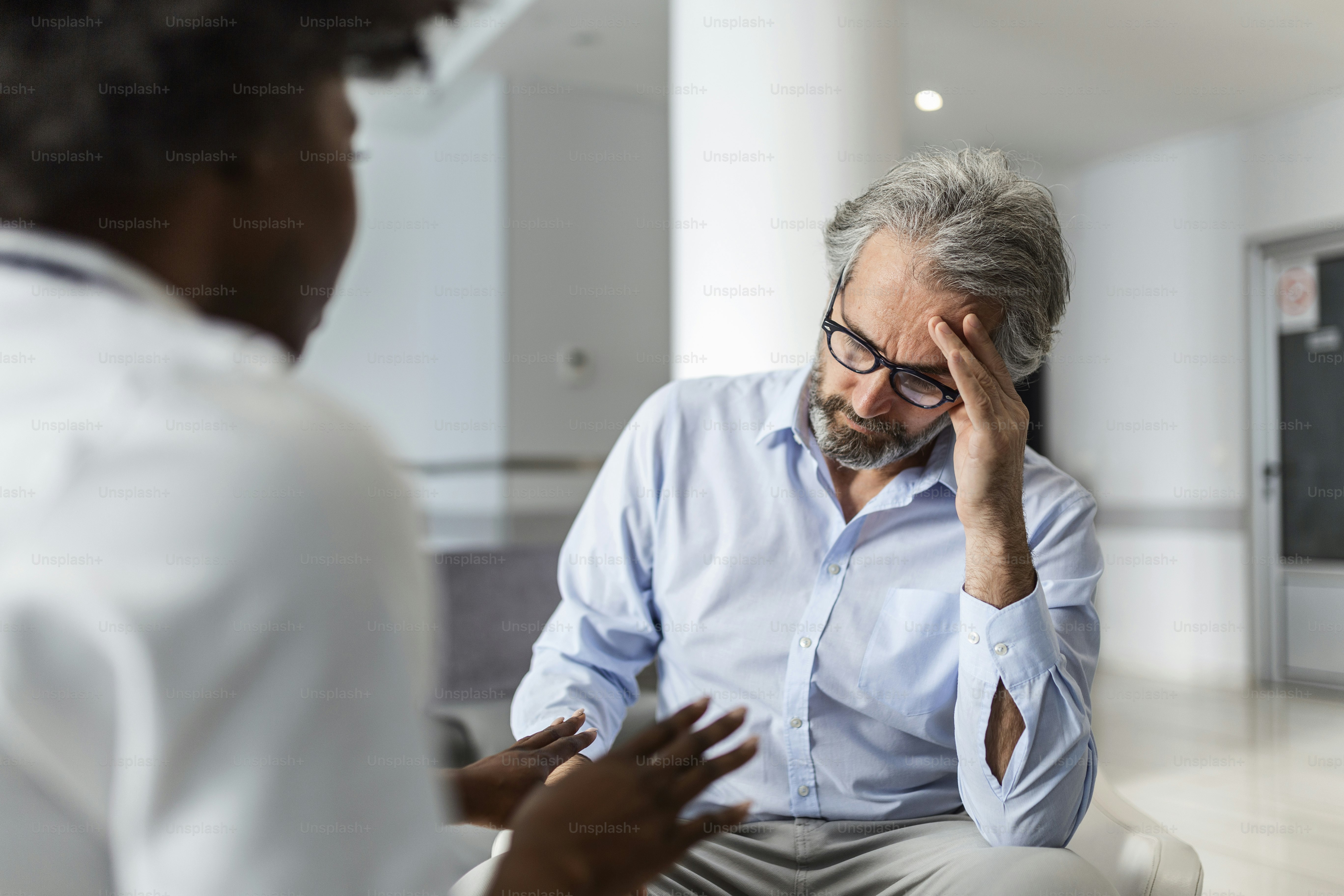 African American doctor talking to a patient who is complaining of headache at the hospital medical clinic. Doctor and patient discussing over report in hospital waiting room