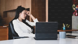 Stressed young businesswoman holding head and sitting in office.