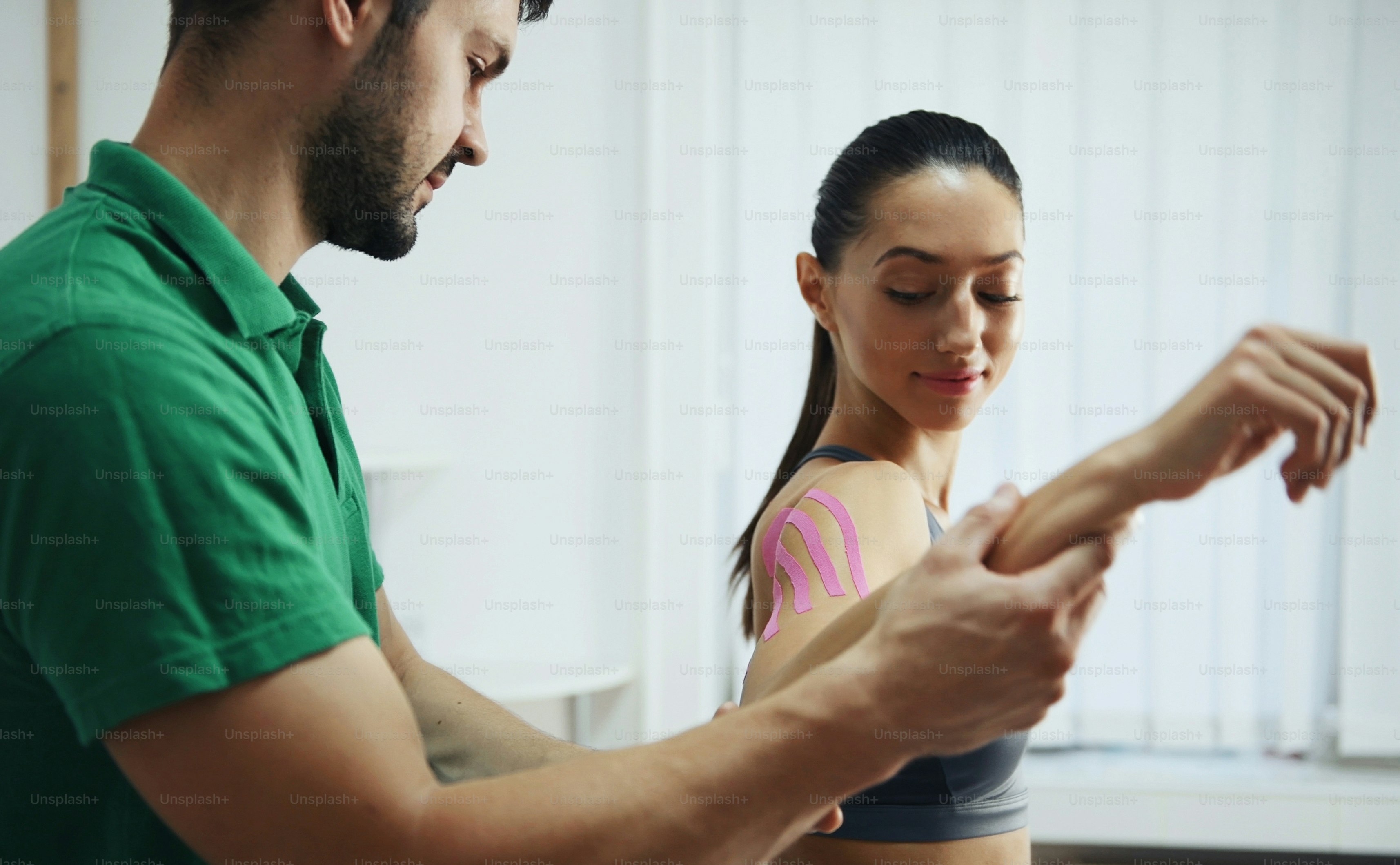 Doctor helps woman by shoulder treatment with kinesio tape.