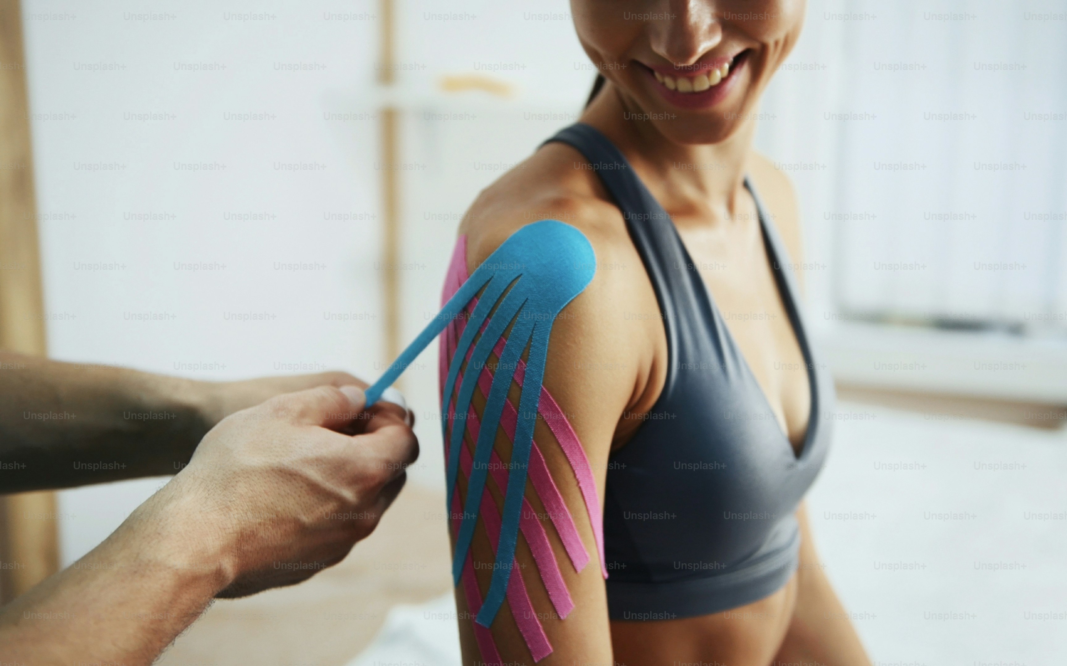 Arzt hilft Frau durch Schulterbehandlung mit Kinesio-Tape