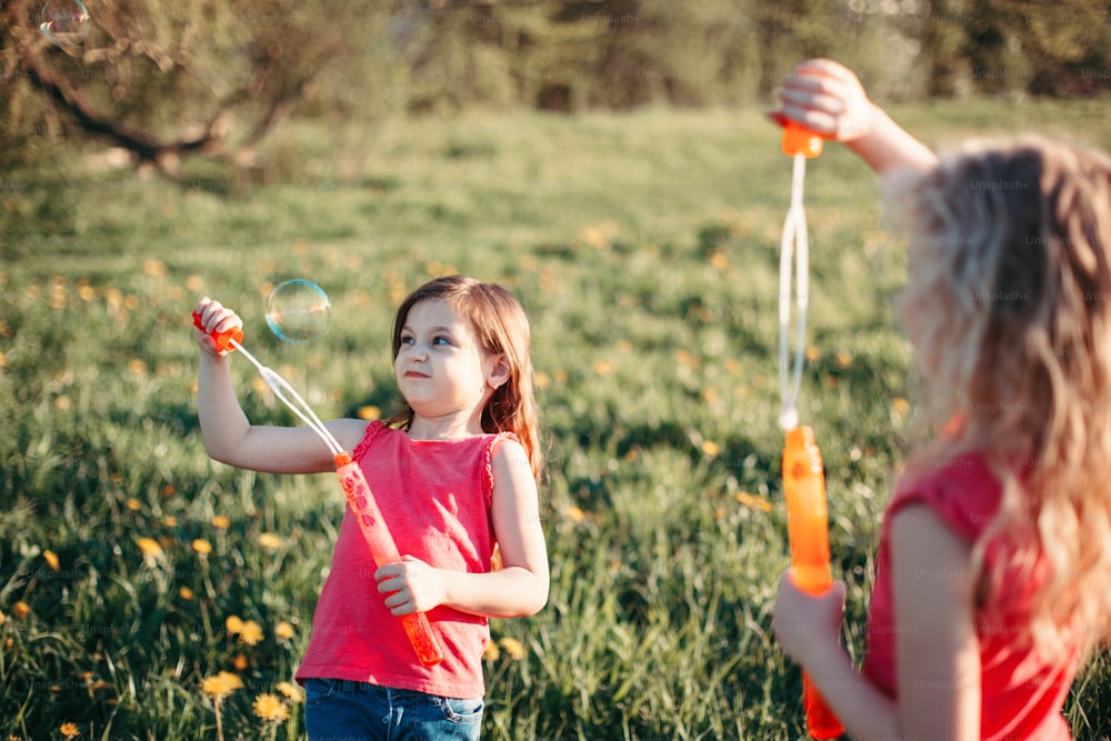 Engraçado momento hilário. Meninas amigas soprando bolhas de sabão no parque no dia de verão. Crianças se divertindo ao ar livre. Autêntico estilo de vida feliz da infância. Atividade sazonal para crianças.