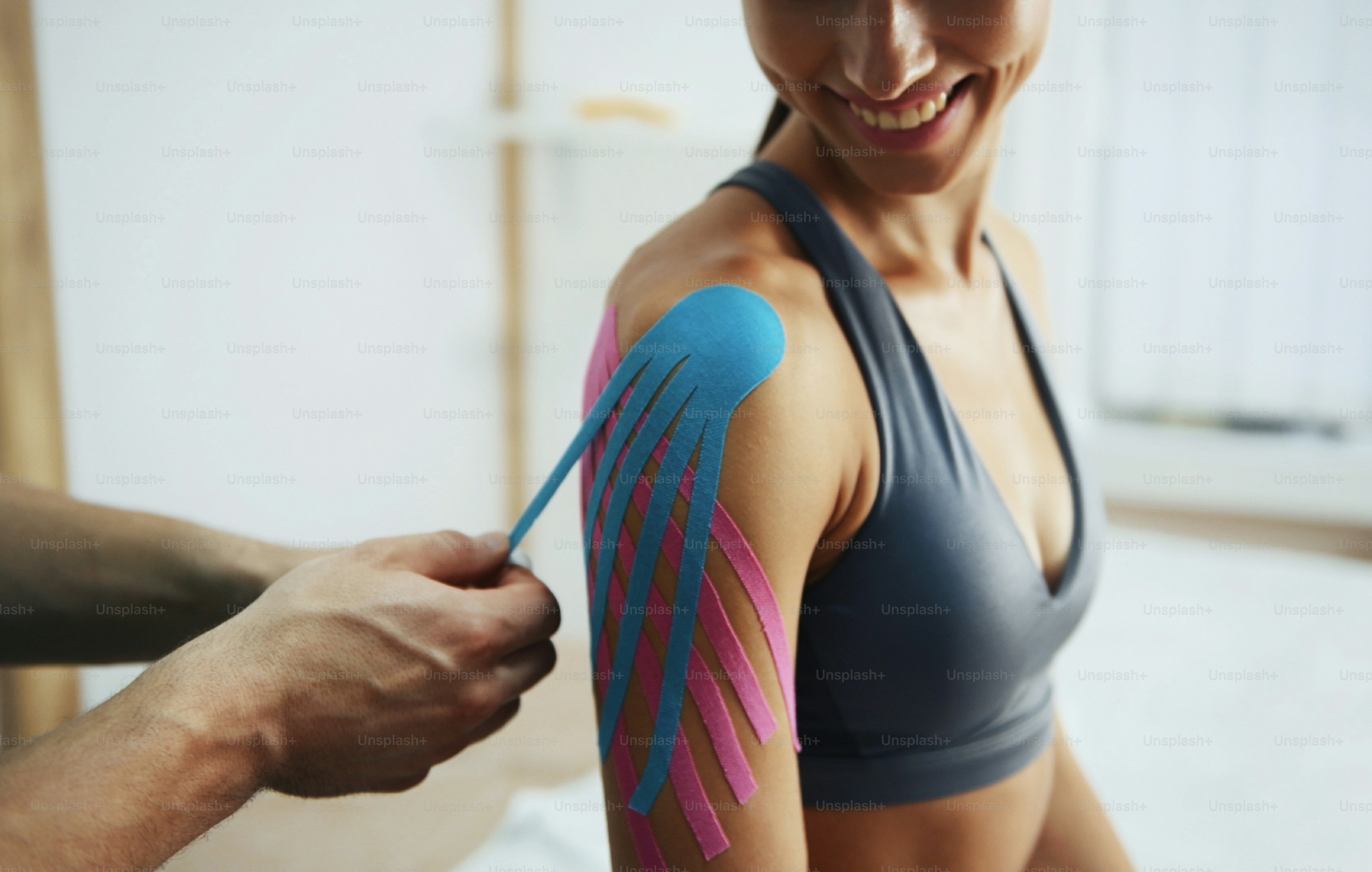 Doctor helps woman by shoulder treatment with kinesio tape.