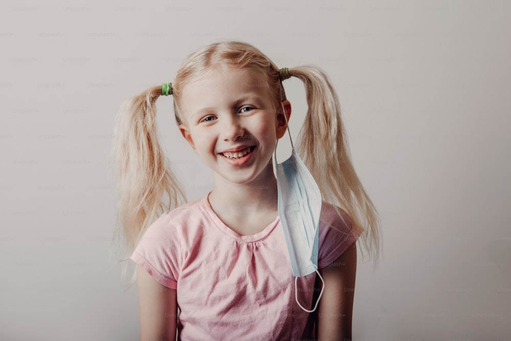 Portrait of Caucasian blonde girl taking off sanitary face mask. Preschool child with protective mask on her ear. End finish of covid-19 quarantine and self isolation concept.