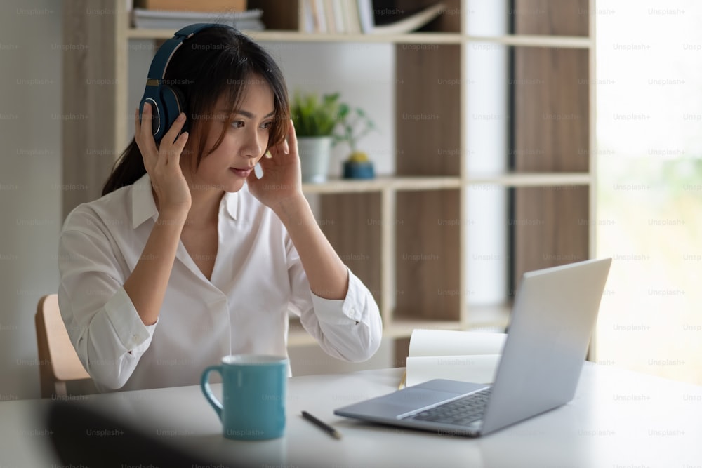 Mulher asiática bonita em fones de ouvido tem chamada de vídeo aula à distância com o professor usando laptop - Conceito de aprendizagem on-line