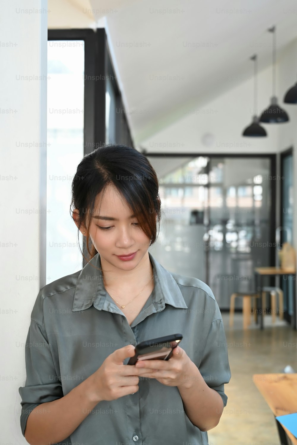 Young asian woman standing in office and using mobile phone.
