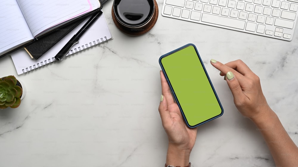 Overhead shot  of woman holding smart phone with green screen on marble background.