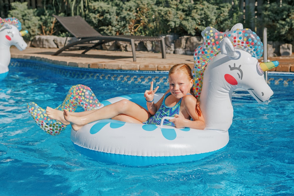 Smiling Caucasian red-haired  girl lying on inflatable ring unicorn. Kid child enjoying having fun in swimming pool. Summer outdoor water activity for kids. Leisure time and rest relax outside.